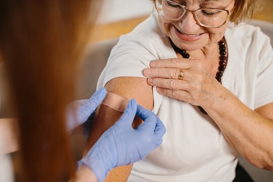 Senior woman receiving vaccination, nurse applying bandage on arm