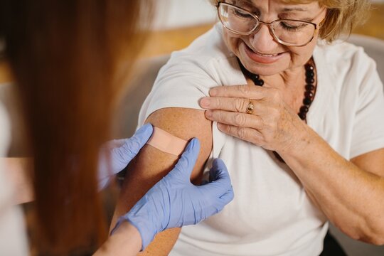 Senior woman receiving vaccine with medical professional applying plaster