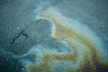 Oil slick on asphalt creating colorful abstract patterns and polluting the environment