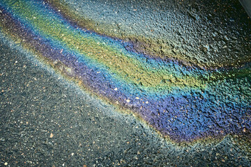 Oil slick reflecting rainbow colors on a wet asphalt pavement, illustrating pollution