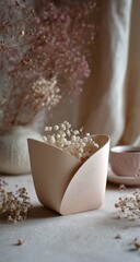 Beige vase filled with small white flowers on neutral surface