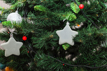 An elegant white ball covered with fine sparkling glitters hangs on a thin silver thread among the thick coniferous branches of a Christmas tree. This minimalist ornament against rich greenery creates