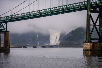 Steel bridge over river with Montmorency Falls in the distance