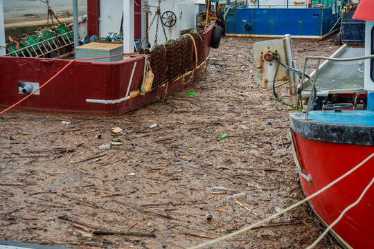 Close-up mud, silt and river debris between fishing boats resting in the port at low tide.