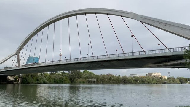 Cable stayed bridge leans over the river under patchy grey clouds with reflections and subtle ripples