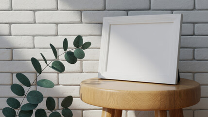 White picture frame on wooden stool with eucalyptus branch against white brick wall