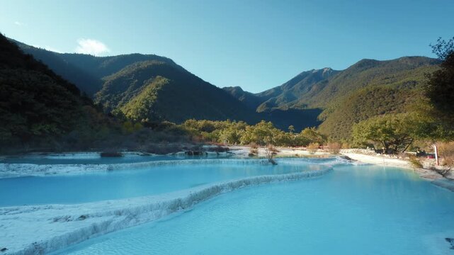Brilliant blue terraced pools of Baishuitai reflect surrounding mountains and forests, revealing a sacred limestone landscape unique to Yunnan, China.