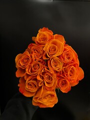 bouquet of a dozen orange colored roses on black background