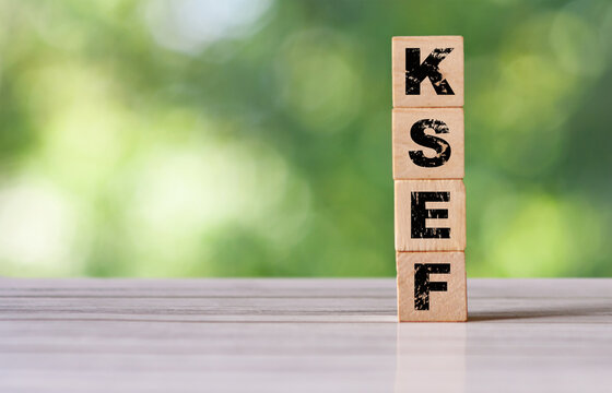 Wooden blocks spelling KSEF are stacked on a light wooden table. The vibrant green background suggests an outdoor setting, making it suitable for concepts related to finance and accounting.