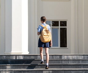 Teen girl with yellow backpack walking up the stairs to classes on sunny morning. Back to school concept