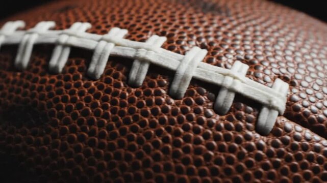 A closeup view of a brown textured sports ball with prominent white lacing across its surface presented with shallow depth of field