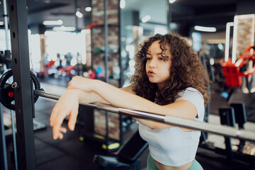 Tired female athlete taking a break, resting her head on a weight bar after intense strength training