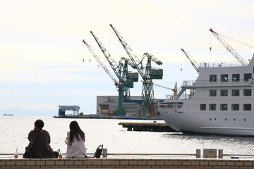 神戸メリケンパークの岸壁に座り海を眺める男女