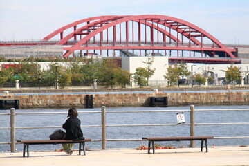 神戸メリケンパークのベンチに座り海を眺める女性と神戸大橋