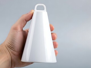 Hand holding a white ceramic cowbell or musical instrument against a light gray background, closeup studio shot