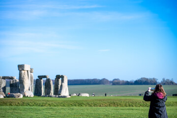 Tourist takes picture of Stonehenge in a sunny day from a distance while other visitors enjoy the site in the background