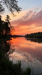 Obraz premium Serene lake at sunset with silhouetted trees and vibrant sky
