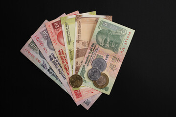 Close-up top view of Indian old rupee notes (INR) and coins of different value on black surface. Concept of cash savings, financial profit and security, Indian economy.