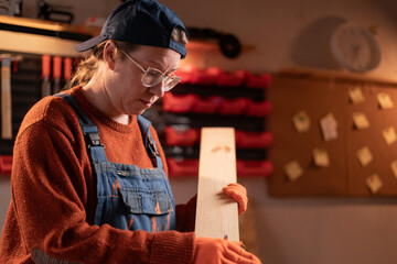 professional carpenter works with wood using carpentry tools in her garage. She holds a laptop and sands a board with sandpaper. Concept of profession, art, and hobby.