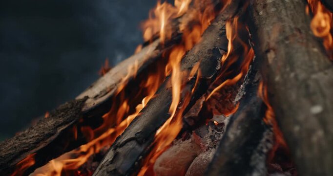 Extreme close up on a shamanic fire shows stacked logs engulfed in bright orange flames, turning rough bark and embers into an intense moving texture of heat. ​