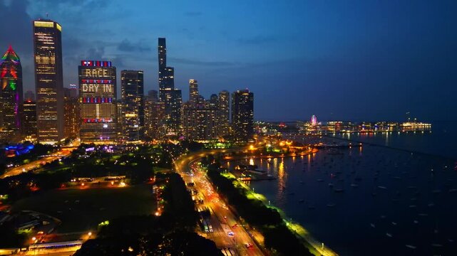 An aerial view captures the vibrant Chicago skyline illuminated at night, with city lights reflecting on Lake Michigan.
