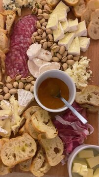 POV of wooden cheese and meat board charcuterie with cured meats pistachios fresh bread gourmet cheeses and apricot jam. Delicious and tasty snack appetizer for friends party. UGC style vertical reel