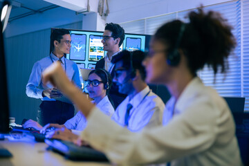 Diverse professional team with headsets working in a modern office. Managers collaborate on digital app data while support staff provide technical assistance at a high-tech communication center.