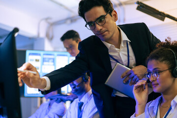 Dedicated professional team collaborates in modern tech office. Manager points at monitor screen while female colleague in headset provides customer support and digital data analysis service