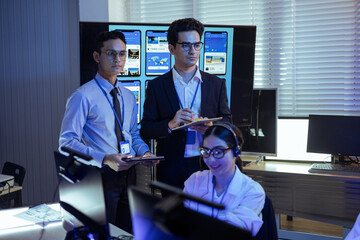 Professional diverse business team and IT specialists working in a high-tech control room or office, monitoring data on large screens and digital tablets during corporate operation