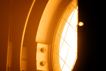Obraz premium Close up of a glowing orange stage spotlight showing metal parts, bolts, and protective wire mesh. Lighting equipment backstage.