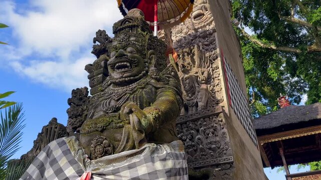 Traditional Balinese stone guardian statues at Hindu temple entrance in Bali, Indonesia. Sacred architecture with symbolic carvings and parasols. Concepts of religon, culture, and travel. 