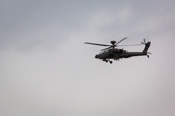 British army AH-64E Boeing Apache attack helicopter flying over Salisbury plain training area during a rain downpour