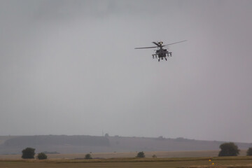 British army AH-64E Boeing Apache attack helicopter flying over Salisbury plain training area during a rain downpour