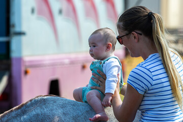 Mother and her baby son, Image shows a young mum in her 20's cuddling her 5 month old baby as he sits on a pony in the shade on a summers day