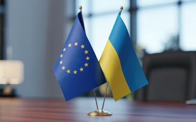 European Union and Ukraine flags standing together side by side on a polished wooden desk in a bright office environment under soft natural light representing international cooperation and political p