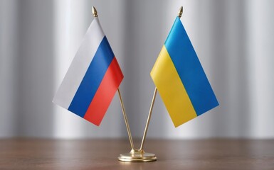 Two small desk flags representing the nations of Russia and Ukraine stand side by side on a polished wooden table indoors with a blurred light grey background under soft even lighting conveying a dipl