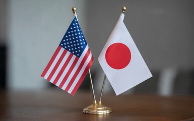 A pair of small desk flags representing the United States of America and Japan stand proudly on a polished wooden table in a well lit indoor setting symbolizing international relations diplomacy and f