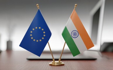 Professional desk display featuring the national flag of India and the European Union flag prominently placed on a warm wooden table in a well lit office setting symbolizing international diplomatic r
