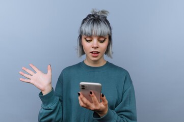 Fototapeta premium Young woman with gray hair looking surprised at smartphone.