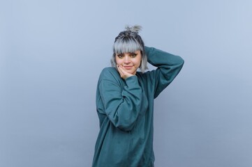 Young woman with gray hair posing playfully against a blue background.