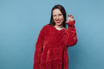 Woman in red sweater playfully posing against blue background.