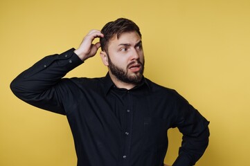 Fototapeta premium Man in black shirt scratching head against yellow background.
