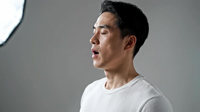 Close-up portrait of a young Asian man with a surprised expression in a plain gray background, capturing a micro moment with soft lighting.