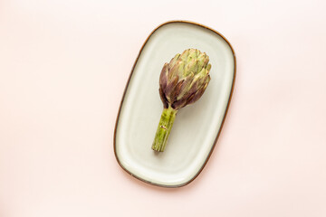 One artichoke flower - purple edible bud on a plate top view. Vegetables food ready to cook
