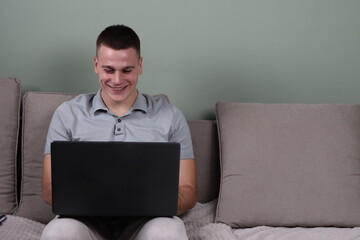 young man sitting on sofa with laptop working from home, male at home office