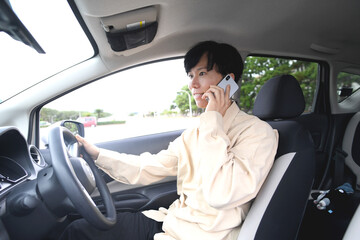 スマホ通話をしながら車を運転する若いアジア人男性
