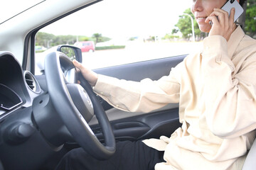スマホ通話をしながら車を運転する若いアジア人男性