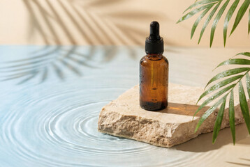 Amber glass dropper bottle on a natural stone podium over water. Minimalist beauty product photography with tropical palm leaf shadows for organic skincare or essential oil branding.