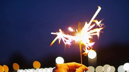 Person holding a sparkler at night with blurred lights in background  