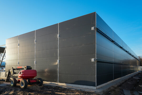 Modern industrial warehouse exterior with installed gray sandwich panel wall under blue sky
